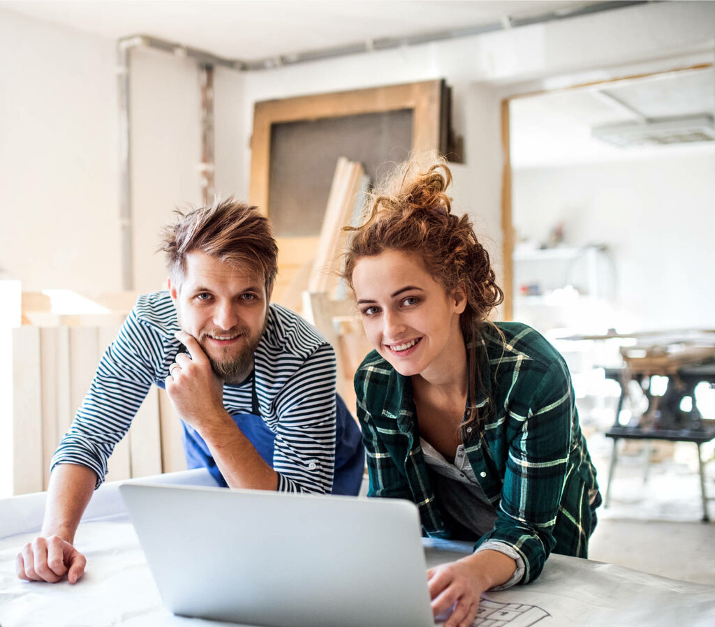 Junges Paar auf einer Baustelle beugt sich über einen Laptop