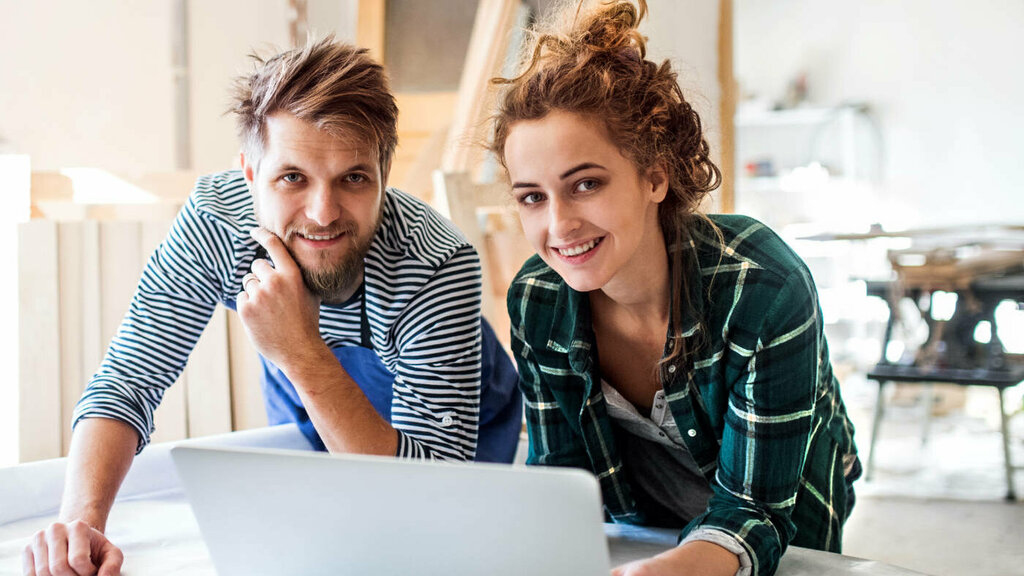 Junges Paar auf einer Baustelle beugt sich über einen Laptop